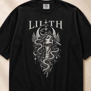 Può includere: Una t-shirt nera a maniche corte con una stampa grafica bianca di una donna con capelli lunghi e serpenti avvolti attorno, posizionata sotto il testo LILITH e una luna crescente. Il design include stelle e spine in un'illustrazione dettagliata.
