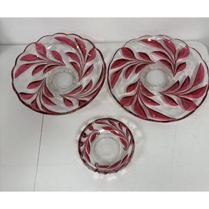 May include: A set of three clear glass serving dishes. The dishes have a scalloped edge and are decorated with a burgundy leaf design. The set includes two large plates and one smaller dish.