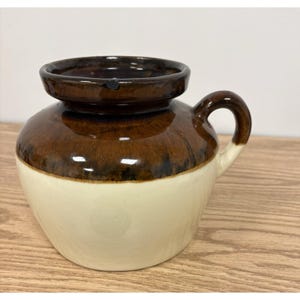 May include: A ceramic shaving mug featuring a two-tone glaze design. The upper portion and handle are finished in a dark brown glossy glaze, while the lower body is a smooth cream color. The mug has a wide, rounded rim and a single side handle.