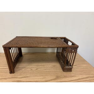 May include: A brown rattan breakfast tray featuring a rectangular surface with a woven cane pattern, a circular cutout for a cup, and vertical slatted supports on each side. The tray has a sturdy frame construction with a natural dark wood finish.