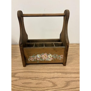 May include: A brown wooden caddy featuring a top handle and four internal compartments. The front panel is decorated with a hand-painted floral design in shades of pink, white, and blue, accented with green leaves and thin, flowing vine details.