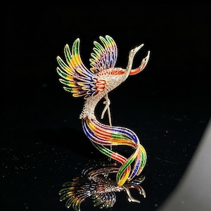 May include: A detailed phoenix brooch. The brooch depicts a bird with outstretched wings and a long, flowing tail. The wings and tail are painted with vibrant colours, including green, yellow, red, and blue. The body is encrusted with sparkling crystals. A beautiful piece of jewellery.