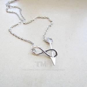 May include: A silver necklace with an infinity symbol and an arrow pendant.