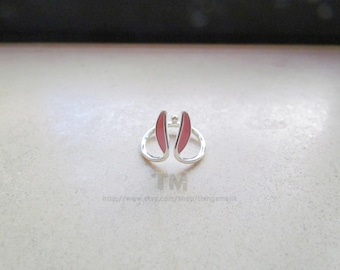May include: A silver ring with pink bunny ears. The ring is on a white surface.