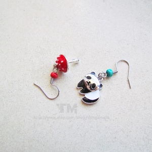 May include: A pair of earrings featuring a red mushroom charm and a panda bear charm. The panda bear charm is silver with black and white details. The mushroom charm is red with white dots. The earrings are silver and have a turquoise bead.