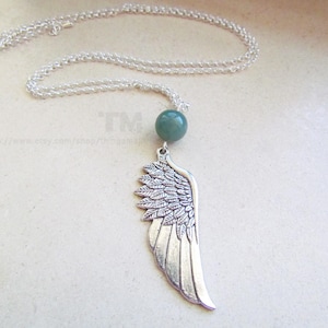 Könnte beinhalten: Eine silberne Halskette mit einem grünen Steinanhänger und einem silbernen Flügel-Anhänger.