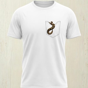 Könnte beinhalten: Weißes T-Shirt mit einer Tasche mit einem Schlangenmuster. Die Schlange ist braun und beige mit einem detaillierten Muster. Das T-Shirt hat kurze Ärmel und einen Rundhalsausschnitt, geeignet für Freizeitkleidung.