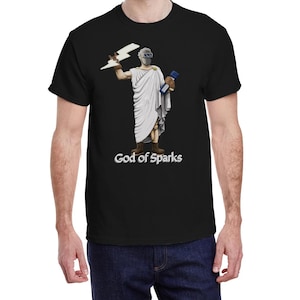 May include: Black t-shirt featuring a graphic of a figure in a toga holding a lightning bolt and a book, with the text "God of Sparks" below. The figure wears a welding mask. The shirt is a classic crew neck.