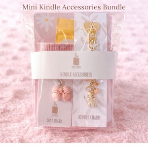 May include: A bundle of Kindle accessories in a clear plastic package. The bundle includes a gold-coloured heart-shaped zip pull, a pink bow dust charm, and a Kindle charm. The package is wrapped with a white band that reads "COZY BEARS KINDLE ACCESSORIES."