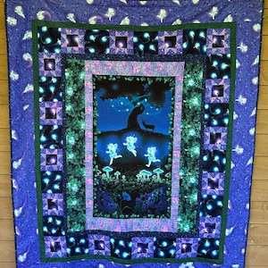 Puede incluir: Un edredón azul y morado con una escena de bosque caprichosa. El centro presenta un árbol, un ciervo y hadas brillantes. El edredón tiene un borde con patrones cuadrados y florales, creando una sensación acogedora y mágica.