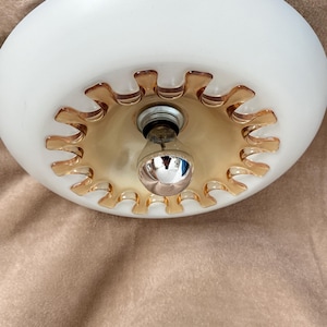 Puede incluir: Una lámpara de techo de vidrio esmerilado blanco con un adorno decorativo de color ámbar. La lámpara tiene forma redondeada y una sola bombilla en el centro. Diseñada para montaje en techo.
