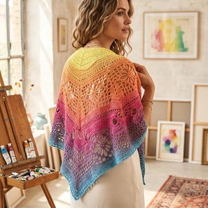 May include: A colorful, crocheted shawl in a gradient of yellow, orange, pink, and blue. The shawl features a floral lace pattern and is worn over a cream-colored dress. The background includes an artist's easel and framed artwork.