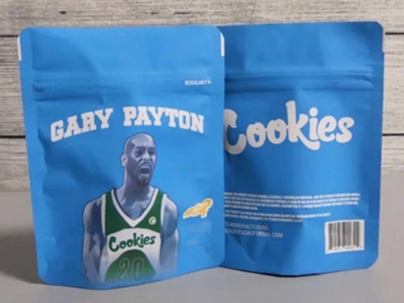 Pode incluir: Duas sacolas azuis, sel&aacute;veis, com o texto "GARY PAYTON" e "Cookies" em branco. Uma sacola apresenta um gr&aacute;fico de um jogador de basquete com uma camisa verde e branca. As sacolas t&ecirc;m um c&oacute;digo de barras e outro texto.