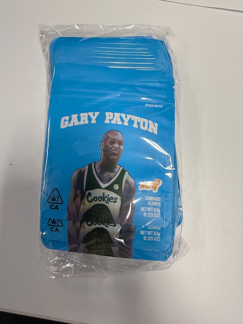 Pode incluir: Uma embalagem azul sel&aacute;vel com o texto "GARY PAYTON" e uma imagem de um jogador de basquete. A embalagem tamb&eacute;m exibe o logotipo "Cookies", s&iacute;mbolos de cannabis e o texto "CANNABIS FLOWER NET WT 3,5g (0,125 OZ)".