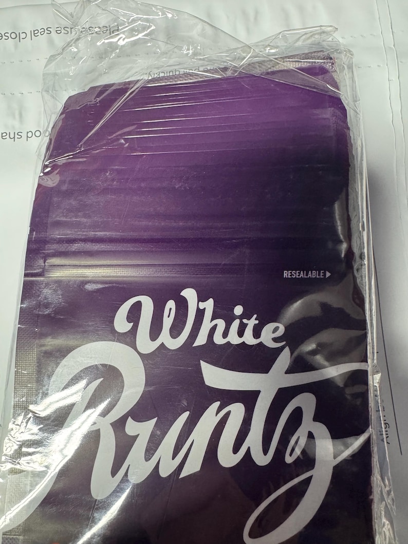 May include: A sealed package with a purple background and the words "White Runtz" in white script. The package is in a clear plastic bag, and the word "RESEALABLE" is visible.