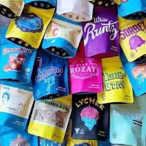 May include: A selection of vibrant, sealed pouches with diverse designs and text. The pouches display text including "Baby Payton," "White Runtz," "Lemonchello," and "Cereal Milk." The pouches are in shades of blue, yellow, purple, pink, and white.