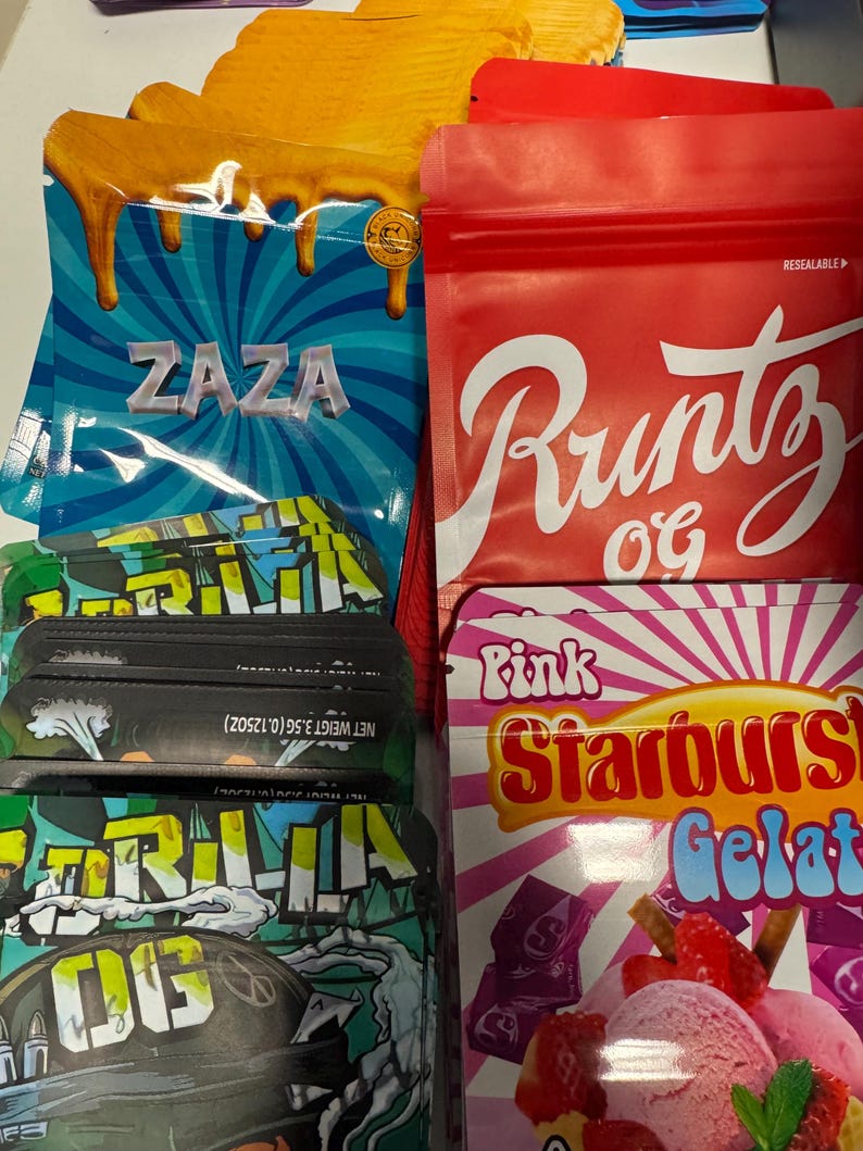 May include: Assortment of colorful resealable bags and boxes. The bags feature the text "ZAZA" on a blue background, "Runtz OG" on a red bag, and "Gorilla OG" on a green bag. A box displays "Pink Starburst Gelato".