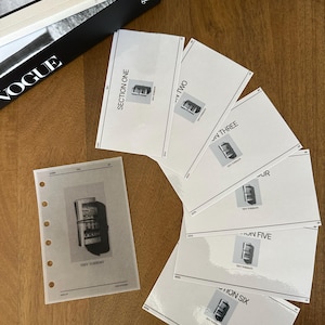 May include: A collection of white cards and a binder page with the text "TINY TUESDAY" and a graphic of a film roll. The cards are labeled "SECTION ONE" through "SECTION SIX". A black and white book with "VOGUE" printed on the cover is in the background.