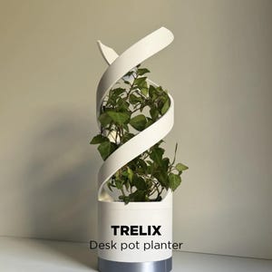 Puede incluir: Una maceta de escritorio blanca con un diseño en espiral, llena de plantas verdes. La maceta tiene una base cilíndrica con una banda plateada en la parte inferior. El texto "TRELIX Desk pot planter" está impreso en la parte delantera.