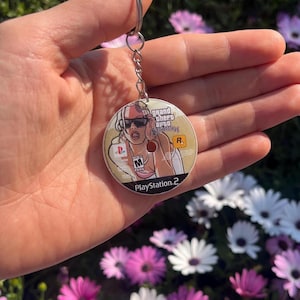 May include: A white ceramic mug with a black handle and the text "But First, Coffee" in a bold, black font. The mug is set against a blurred background. The mug appears to be approximately 10 cm tall.