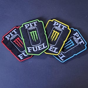 May include: Four embroidered patches featuring a black background with a central energy drink can graphic and the text PIT FUEL. Each patch has a distinct border colour: red, lime green, yellow, and light blue, with matching coloured claw logos.