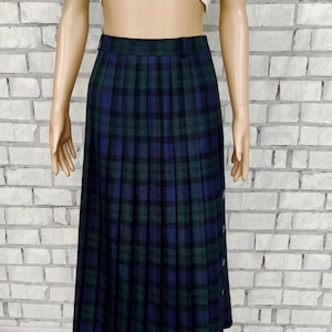 May include: A pleated midi skirt in a blue and green plaid pattern. The skirt has a button closure on the side and is paired with a white, ruffled crop top. The skirt is knee-length and has a classic, timeless design.