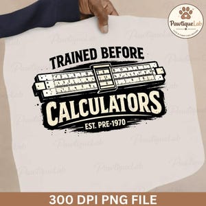 May include: A white t-shirt design featuring a black and white graphic of a slide rule with the text "TRAINED BEFORE CALCULATORS EST. PRE-1970". The design is held up by a person's hand.