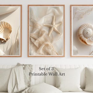 Pode incluir: Conjunto de três impressões de arte de parede emolduradas com conchas e uma estrela do mar. As impressões têm uma paleta de cores neutras com tons bege e creme. As molduras são de cor castanho claro. O texto "Set of 3 Printable Wall Art" é visível.