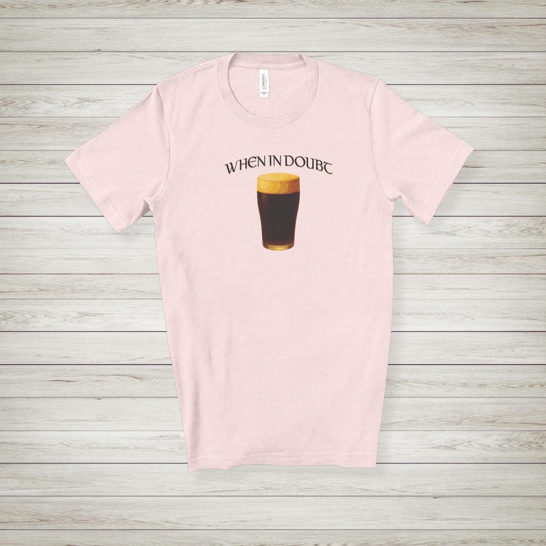 May include: Light pink t-shirt with the phrase "WHEN IN DOUBT" above a graphic of a pint of dark beer with a foamy head. The shirt is made of a soft material and has a crew neck.