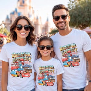 Peut inclure: T-shirts blancs avec un graphisme color&eacute; de personnages de Cars et le texte "Radiator Springs". Les chemises sont port&eacute;es par une famille de trois personnes, avec le texte et le graphisme au centre des chemises.