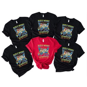 以下が含まれることがあります： 「Buzz & Woody Lightyear To Infinity And Beyond」のテキストと漫画のキャラクターが描かれた、黒と赤のTシャツのコレクション。青と緑の配色です。