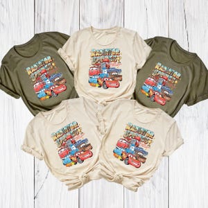 Peut inclure: Cinq t-shirts de couleur vert olive et cr&egrave;me. Chaque t-shirt pr&eacute;sente un graphisme color&eacute; de voitures de dessins anim&eacute;s avec le texte "Radiator Springs Speedway". Le design comprend Flash McQueen et d'autres personnages.