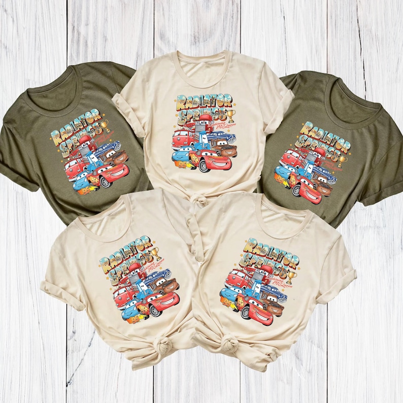 Peut inclure: Cinq t-shirts de couleur vert olive et cr&egrave;me. Chaque t-shirt pr&eacute;sente un graphisme color&eacute; de voitures de dessins anim&eacute;s avec le texte "Radiator Springs Speedway". Le design comprend Flash McQueen et d'autres personnages.