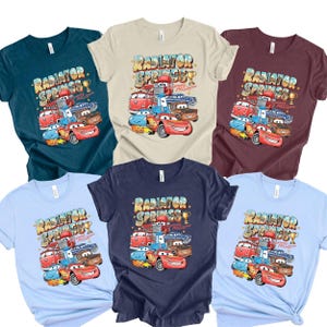 Peut inclure: Plusieurs t-shirts de diff&eacute;rentes couleurs, chacun avec un graphisme des personnages du film Cars. Le design comprend le texte "Radiator Springs" et des images de Flash McQueen et d'autres v&eacute;hicules.