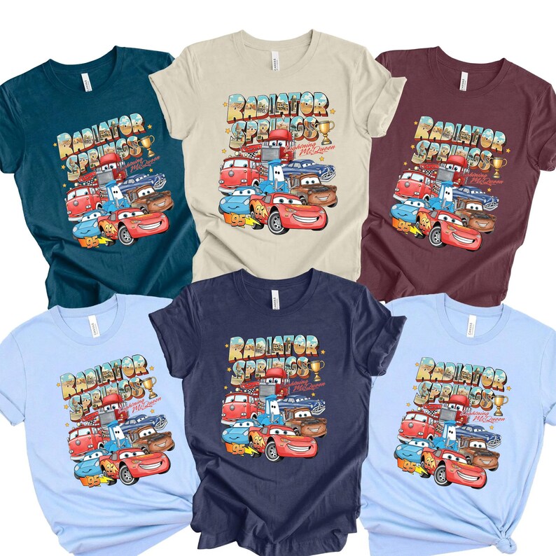 Peut inclure: Plusieurs t-shirts de diff&eacute;rentes couleurs, chacun avec un graphisme des personnages du film Cars. Le design comprend le texte "Radiator Springs" et des images de Flash McQueen et d'autres v&eacute;hicules.