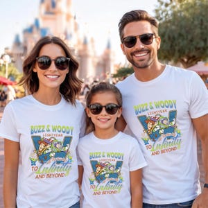 以下が含まれることがあります： 3人の人が、トイ・ストーリーのバズ・ライトイヤーとウッディが描かれたカラフルなグラフィックの白いTシャツを着ています。「BUZZ & WOODY LIGHTYEAR」と「TO INFINITY AND BEYOND」の文字もシャツに表示されています。3人ともサングラスをかけています。