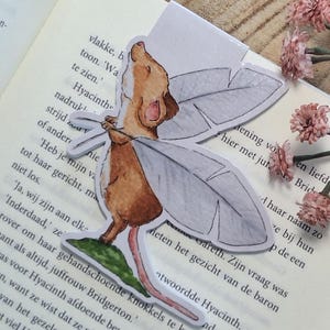 Peut inclure: Marque-page décoratif avec une illustration de souris ailée sur un livre ouvert. Des clés anciennes et des fleurs roses complètent la scène, créant une ambiance vintage et littéraire.