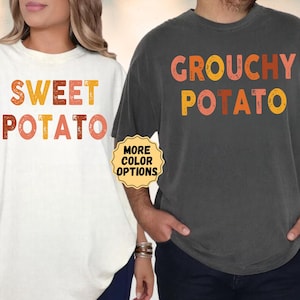 May include: A cream-colored t-shirt with the text SWEET POTATO in orange, yellow, and brown letters, and a charcoal gray t-shirt with the text GROUCHY POTATO in orange, yellow, and brown letters. A small yellow badge reads MORE COLOR OPTIONS.