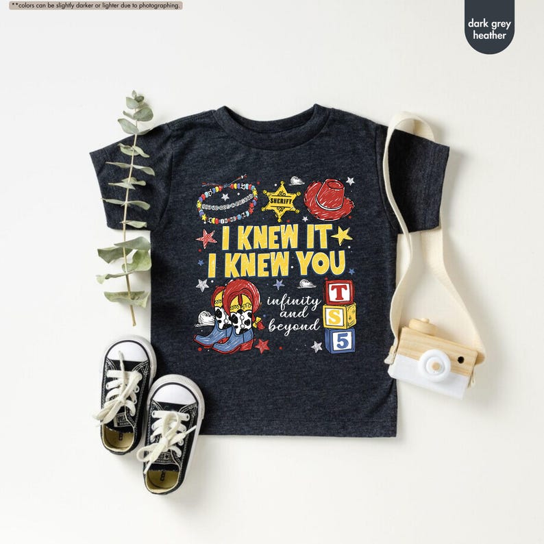 Puede incluir: Una camiseta gris jaspeado oscuro con un estampado gr&aacute;fico con el texto I KNEW IT I KNEW YOU, infinity and beyond, una insignia de sheriff, un sombrero de vaquero rojo, una pulsera de cuentas, botas vaqueras y tres cubos con letras T, S, 5.