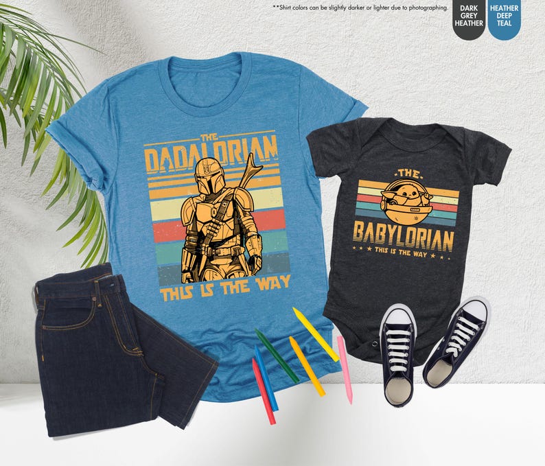 以下が含まれることがあります： 「The Dadalorian」のグラフィックが入った水色のTシャツと、「The Babylorian」のグラフィックが入った濃いグレーのベビーボディスーツ。どちらも、キャラクターのイラストと「This is the Way」というフレーズが入ったレトロなデザインです。濃い青色のジーンズと黒いスニーカーも画像にあります。