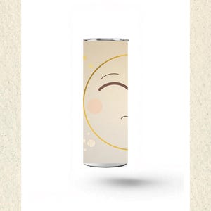 May include: A cylindrical tumbler with a beige background featuring a partial gold-lined circle, a brown curved line representing an eye, a small pink circle for a cheek, and scattered gold stars. The text Fusion Artistry Collection NZ is below.