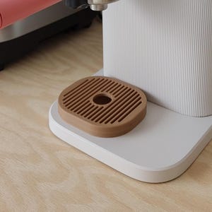 Könnte beinhalten: Eine weiße Philips Baristina Espressomaschine mit rosa Griff und Holz-Abtropfschale. Die Maschine hat eine silberne Zierleiste und einen Behälter oben. Links befindet sich ein Edelstahlgerät.
