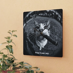 May include: Square wall clock featuring a black and white image of a cat holding a cigar. The cat is looking up at the viewer. The clock hands are black. The text "Print it your way" is at the bottom of the clock.