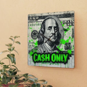 May include: Square wall clock featuring a design of a US $100 bill with Benjamin Franklin's portrait. The clock face has green paint splatters and the words "CASH ONLY" in a graffiti style font. The clock hands are black.