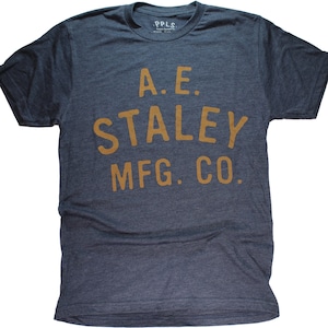 May include: A dark blue t-shirt with a vintage-style logo printed in gold. The logo reads "A.E. STALEY MFG. CO."