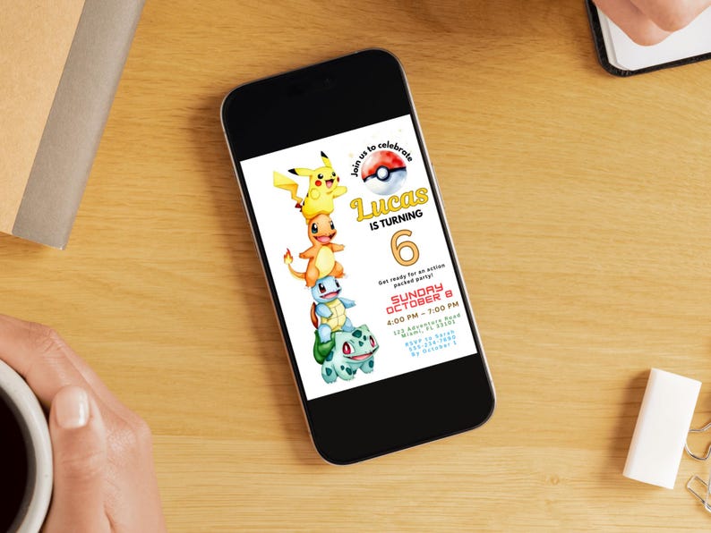 May include: A smartphone displays a birthday party invitation featuring stacked cartoon characters. The invitation reads "Lucas is turning 6" with event details. The phone rests on a wooden surface, with a coffee cup and stationery nearby.