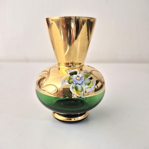 Könnte beinhalten: Eine kleine, dekorative Vase mit goldfarbenem Ober- und Unterteil und einem grünen Mittelteil. Die Vase hat ein handgemaltes Blumendesign mit blauen, gelben und grünen Akzenten. Die Vase hat einen runden Körper und einen ausgestellten oberen Teil.