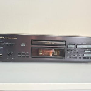 Può includere: Un lettore di compact disc Onkyo DX-7511 nero dotato di un vassoio centrale per il disco, una finestra con display digitale, un pulsante di accensione, un jack per cuffie, una manopola del livello di uscita e vari pulsanti di controllo.
