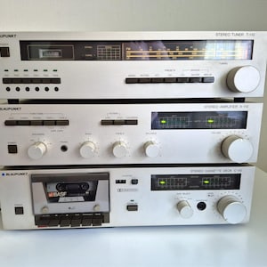 Puede incluir: Una pila de tres componentes de audio Blaupunkt plateados que incluye un sintonizador estéreo T-110, un amplificador estéreo A-110 y una platina de casete estéreo C-110. Cada unidad presenta un acabado metálico, perillas y botones.