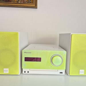 May include: A Pioneer stereo system consisting of a central unit and two speakers. The speakers have bright lime green fabric grilles and white cabinets. The central unit features a lime green front panel, a digital display, and a large volume knob.